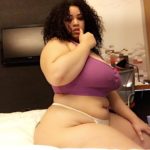 Grosse métisse assise sur son lit avec cheveux frisé